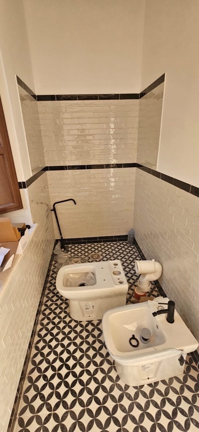 Bagno finito con sanitari, rivestimento a fascia scura e pavimento in cementine geometriche